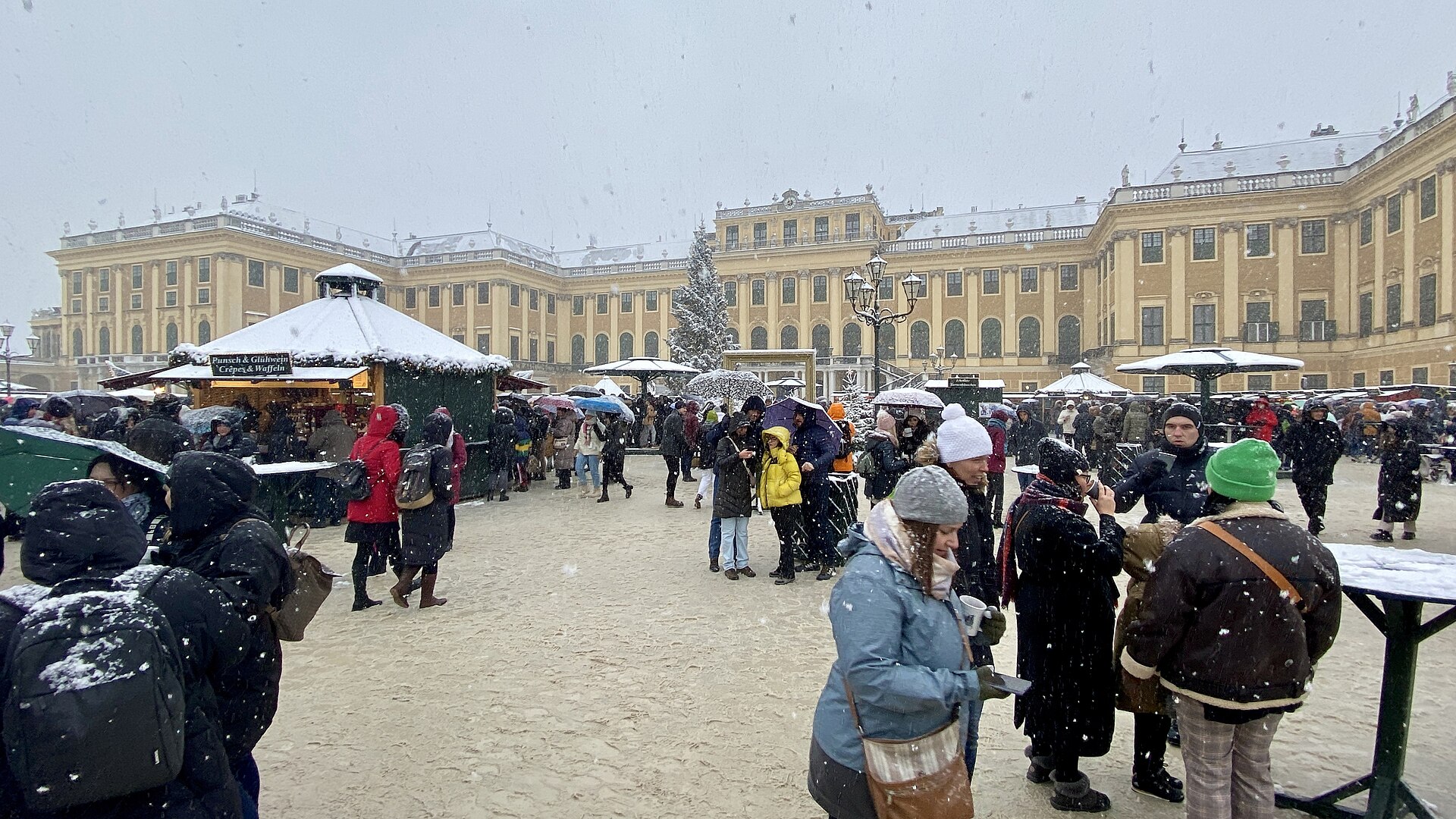 Visitors in the snowy Schönbrunn Palace courtyard during a Christmas market